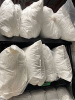 Three shelves filled with white bed pillows in clear plastic bags
