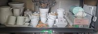 Full shelf showing assorted white ceramic items, wire fruit bowl, boxed cups