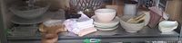 Shelf view showing majority of dinnerware, glass bowl set, wood board, linens and ceramic pieces