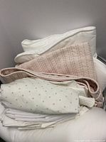 Stack of blush quilted coverlet, polka dot sheet and additional white linens