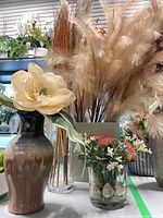 Group shot showing pampas grass in grey vase, gradient ceramic vase with cream flower, small glass succulent arrangement