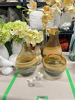 Group shot of three swirl glass vases, both orchid arrangements, tan ceramic vase and ceramic birds