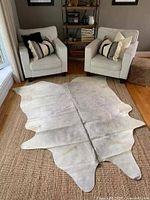 Full view of white cowhide rug on woven area rug between two chairs