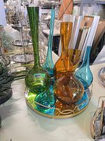 Overall lot showing six coloured glass vases arranged on gold metal mirrored tray