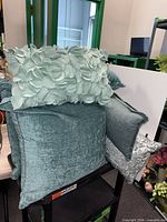 Group of teal chenille, pale aqua applique, and grey damask pillows on cart
