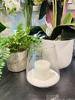 Artificial orchid, faux fern, glass candle holder grouped on shelf