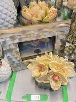 Square glass cube with faux cymbidium orchids in front of silver wave photo frame, tulip arrangement partially visible