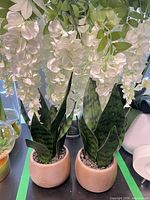 Two faux snake plants in ceramic pots beneath hanging white faux flowers