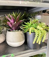 Shelf with two faux succulent arrangements in grey and black pots