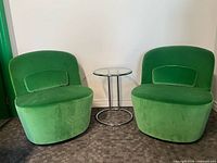 two green velvet swivel chairs and glass side table