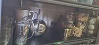 Full shelf view showing assortment of watering cans, jars, vase, mister, mug, canister
