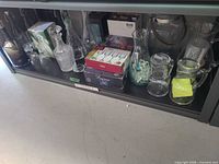 Shelf holding assorted glass decanters, carafes, pitcher, stein, boxed items