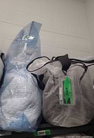 Two storage bags holding pewter coverlet and white quilted coverlet set