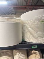 Two white drum lamp shades on shelf, one partially in plastic wrap