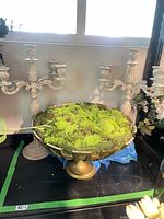 gold-tone pedestal bowl with faux moss flanked by two ceramic candelabras
