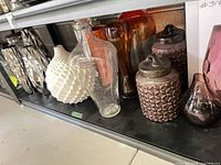 shelf with multiple vases including white geometric, clear speckled, amber, silver mirrored and purple canisters