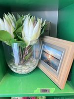 Floraseda faux protea arrangement in glass vase beside wood frame
