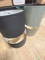 Stacked view of two charcoal grey and two sage green drum lamp shades