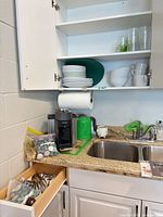 Cabinet with plates, bowls, mugs, glasses; kettle on counter; cutlery drawer