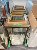 Two lantern lids and bodies showing copper frames, wooden tops, glass sides, pebble bases