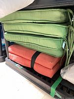 Stack of three green and two orange seat cushions on shelf