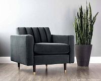 Angled view of smoke grey channel-tufted armchair with plant for scale