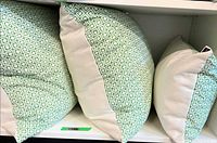 Three pillows on shelf showing front patterned panels and size relation