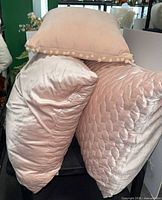 Three blush pink pillows stacked, showing pom-pom trim and quilted patterns