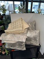 Stack of decorative pillows with swirl and stripe covers alongside folded champagne quilted throw