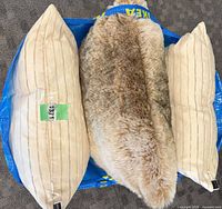 Three pillows in Ikea bag: two beige striped, one faux-fur