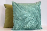 Front view of square pillow in turquoise/gold pattern with olive pillow behind