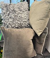 Group of pillows showing grey petal appliqué, light grey-green woven, taupe velvet with piping, and dark grey velvet with piping