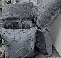Stacked view of five blue-grey pillows and folded throw blanket