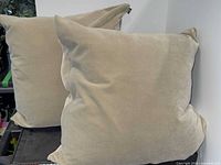 Two beige square pillows standing upright on shelf