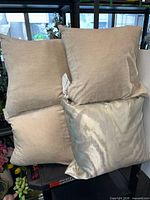 Group shot of five pillows stacked showing four solid beige and one patterned cushion