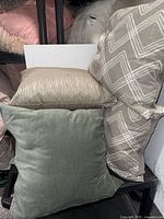 Three of the pillows: solid sage green, taupe geometric, taupe stripe, stacked on shelving