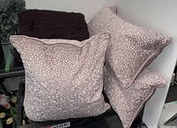 Group view: three pink pillows stacked and one burgundy throw folded on cart