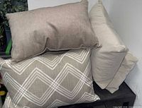 Stacked decorative pillows: taupe, patterned grey, and cream