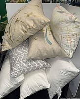 Stack of assorted pillows showing twig print, typography pillow, herringbone pillow, two white pillows, bird pillow