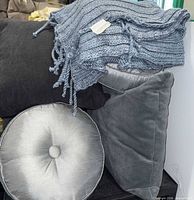 stack of pillows showing charcoal, grey velvet, silver round pillow and knit throw