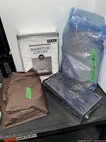 Packaged Hampton Luxury queen sheet set, grey sheet in blue bag, luxe habitat fitted sheet, brown sheet folded