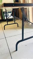 Side view of black metal folding legs and frame under tabletop