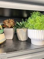 Three faux plants in ceramic pots: square beige, faceted grey, white ribbed