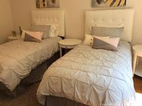 Both twin beds made with grey ruched comforters and accent pillows