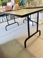 Table full view showing beige laminate top and black folding legs