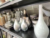 Shelf with assorted silver and mercury-glass vases, bottles and white glass pieces