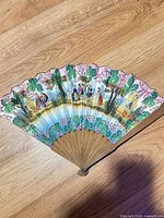 Full view of opened fan showing painted scene and wooden sticks