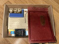 Overview of box showing red photo album, small book, loose photos and ephemera