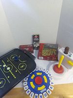 Group shot of all games including Tapple disc, Exploding Kittens box, Chinese Checkers box, dominoes box, air hockey board, Flushin' Frenzy pieces