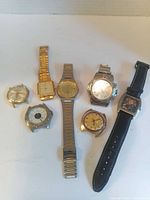 Seven wristwatches laid out showing mix of bracelet and strap types
